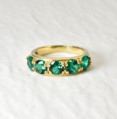 a gold ring with green stones on it sitting on a white surface in front of a plain background