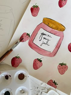 a jar of jam with strawberries painted on it next to some paintbrushes