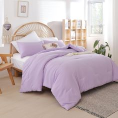 a bed with purple comforter and pillows in a room next to a plant on the floor