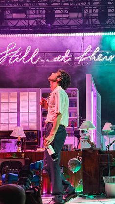 a man standing on top of a stage in front of a purple lit sign that reads still at home