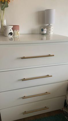 a white dresser with gold handles and knobs next to a vase with yellow flowers