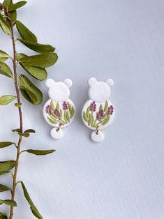 two white teddy bears with green leaves and purple flowers on them, sitting next to each other