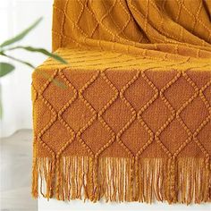 an orange blanket sitting on top of a wooden table next to a plant in a vase