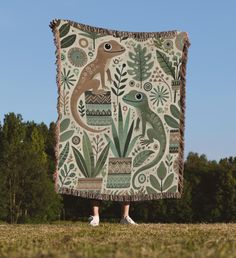 a person standing in the grass with a blanket on their back that has an image of a lizard and plants