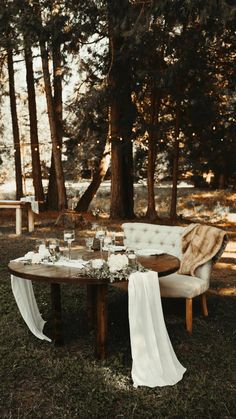 a table set up with white linens and flowers for an outdoor wedding reception in the woods