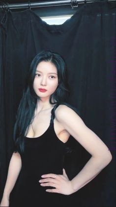 a woman with long black hair standing in front of a black curtain and posing for the camera