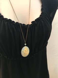 "Here is a beautiful blue lily of the valley cameo necklace. This is a large cameo which features nicely detailed lily of the valley flowers against a dreamy blue background. This cameo is set in an oxidized brass setting and is suspended from one Czech glass bead along with a high quality long brass chain. All materials are lead and nickel safe, cameo is resin. Handcrafted in the USA by Botanical Bird. This necklace comes shipped in a lovely gift box. Cameo Pendant measures: 1 1/4\" across x 1 Blue Locket Necklace For Wedding, Blue Medallion Necklace For Wedding, Blue Medallion Necklaces For Wedding, Blue Cameo Jewelry For Wedding, Antique Blue Necklace With Vintage Charm, Victorian Blue Cameo Jewelry, Antique Blue Necklaces With Vintage Charm, Blue Victorian Jewelry With Vintage Charm, Blue Cameo Necklace For Wedding