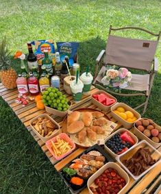 a picnic table filled with lots of food and drinks on top of grass next to a lawn chair