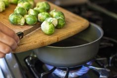 a person cutting brussels sprouts on a cutting board next to an electric stove