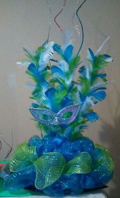 a blue and green centerpiece with feathers, streamers and ribbons on a table