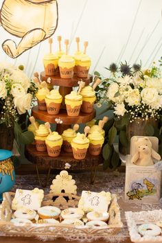 a table topped with lots of cupcakes covered in yellow frosting next to flowers