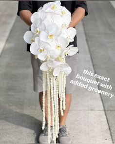 a person is holding a bouquet with white orchids and pearls on the side walk