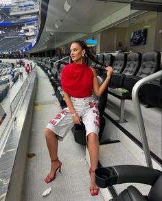 a woman sitting in the bleachers at a baseball game wearing red and white