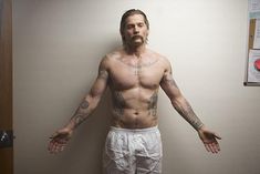 a shirtless man with tattoos standing in front of a wall