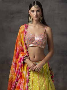 This yellow banarsi mixed panelled lehenga is paired with a rainbow mirror work choli.  The outfit is completed with a stunning tie-dye dupatta. Yellow Lehenga With Mirror Work For Navratri, Anarkali Yellow Sharara With Bandhani Print, Yellow Anarkali Sharara With Bandhani Print, Navratri Yellow Lehenga With Mirror Work, Fitted Yellow Choli With Mirror Work, Yellow Choli With Mirror Work For Diwali, Bollywood Yellow Choli With Mirror Work, Anarkali Choli With Mirror Work In Yellow, Traditional Yellow Bandhani Print Choli