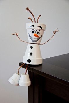 a snowman made out of cups on top of a wooden table next to a white wall