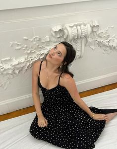 a woman sitting on top of a bed in a black and white polka dot dress