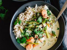 a bowl filled with rice and vegetables on top of a black table next to a spoon