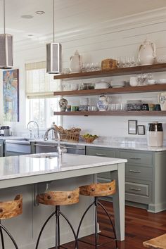 a kitchen with wooden stools and open shelving on the wall above the island