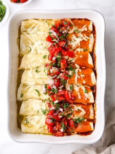 an enchilada with tomatoes, onions and cheese in a white casserole dish