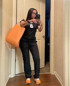 a woman taking a selfie with her cell phone in front of the door while holding an orange purse