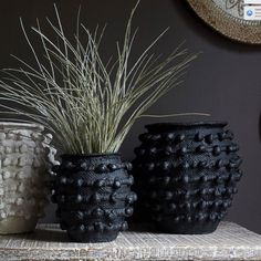 three black vases with grass in them on a table next to a mirror and clock