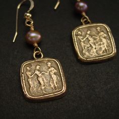 the earrings are decorated with an image of people on them and pearls hanging from them