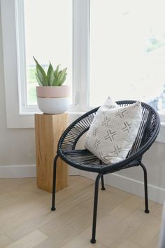 a black chair sitting in front of a window next to a potted plant on top of a wooden table