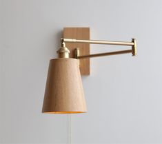 a wall light with a wooden shade hanging from it's side on a white wall