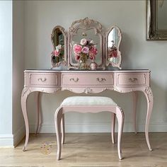 a pink vanity with mirror, stool and flowers