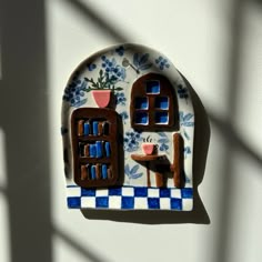 a blue and white plate with a small house on it's side next to a window