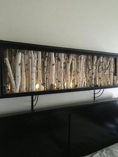 candles are lit in between the branches of a birch tree wall hanging above a bed