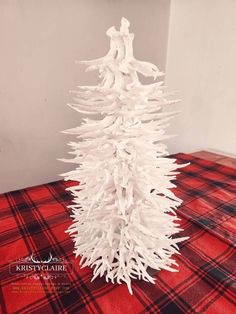 a white christmas tree on a red and black checkered tablecloth with snow falling around it