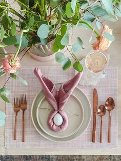 a place setting with pink napkins, silverware and greenery on the table