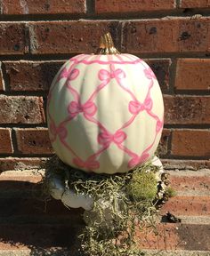 a white pumpkin with pink bows on it sitting in front of a brick wall