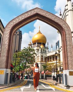 a woman standing in front of an arch with a golden dome on it's top