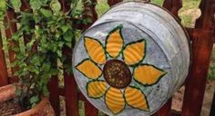 a metal bucket with yellow flowers painted on it sitting in front of a wooden fence