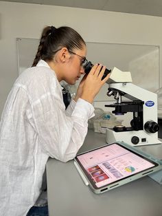 a woman is looking through a microscope at something on her tablet computer and holding it up in front of her face