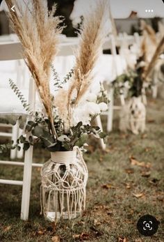 an arrangement of flowers and plants in a vase on the ground at a wedding ceremony