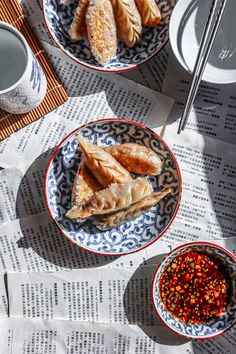 two plates filled with food sitting on top of a newspaper next to cups and saucers