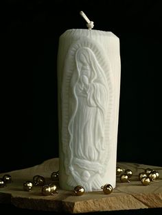 a white candle with an image of jesus on it sitting on a rock surrounded by gold balls