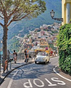 people are walking down the street in positanoo, italy with mountains in the background