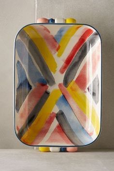 a hand holding a multicolored square shaped dish with handles and two fingers on the handle