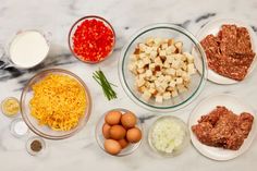 an assortment of ingredients are displayed on a marble counter top, including eggs, cheese and other foodstuffs