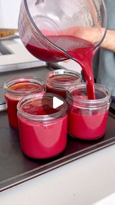 a person pouring red liquid into small jars