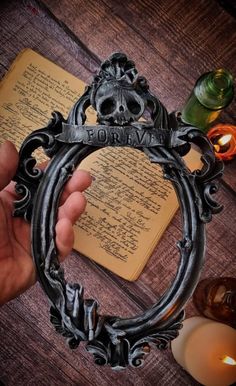 a person holding a metal frame with a skull on it next to candles and an open book