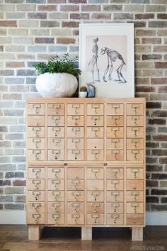 a large wooden cabinet with drawers and pictures on it next to a brick wall in a living room