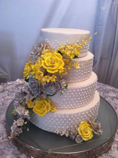 a three tiered wedding cake with yellow and gray flowers on the top, sitting on a silver platter