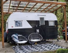 an rv is parked under a pergolated area with chairs and a rug on the ground