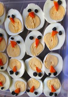 an assortment of deviled eggs with carrots and black olives on them in a plastic container